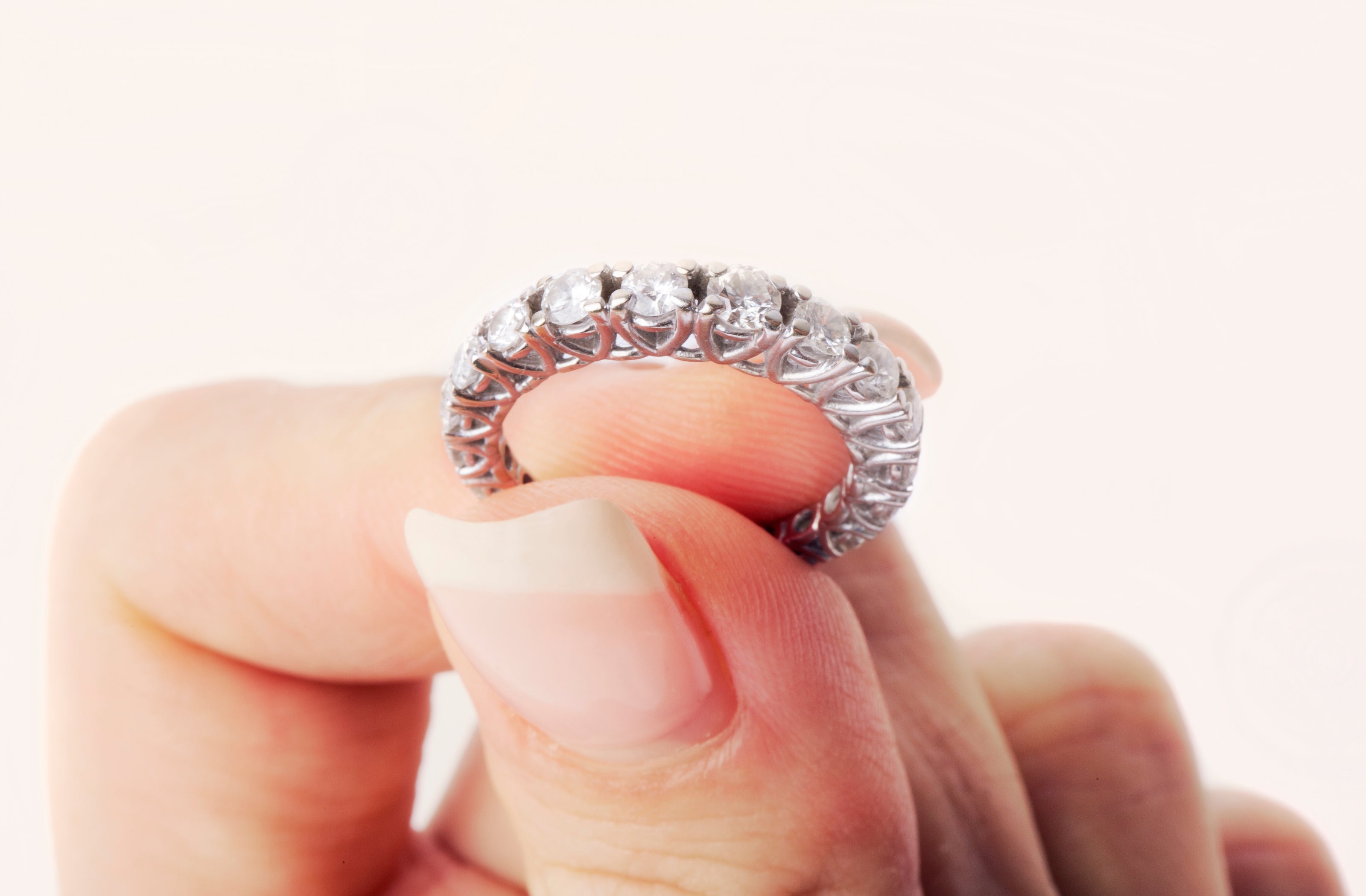 Diamond ring held between fingers against a white background